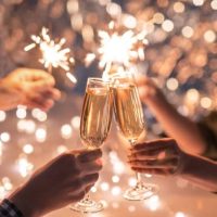 Hands of couple clinking with flutes of champagne and their friends holding sparkling bengal lights