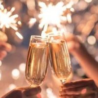 Hands of couple clinking with flutes of champagne and their friends holding sparkling bengal lights