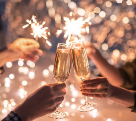 Hands of couple clinking with flutes of champagne and their friends holding sparkling bengal lights